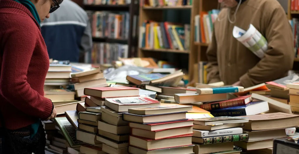 Stand de troc de livres organisé par genre avec signalétique artisanale sur tables en bois, ambiance brocante culturelle